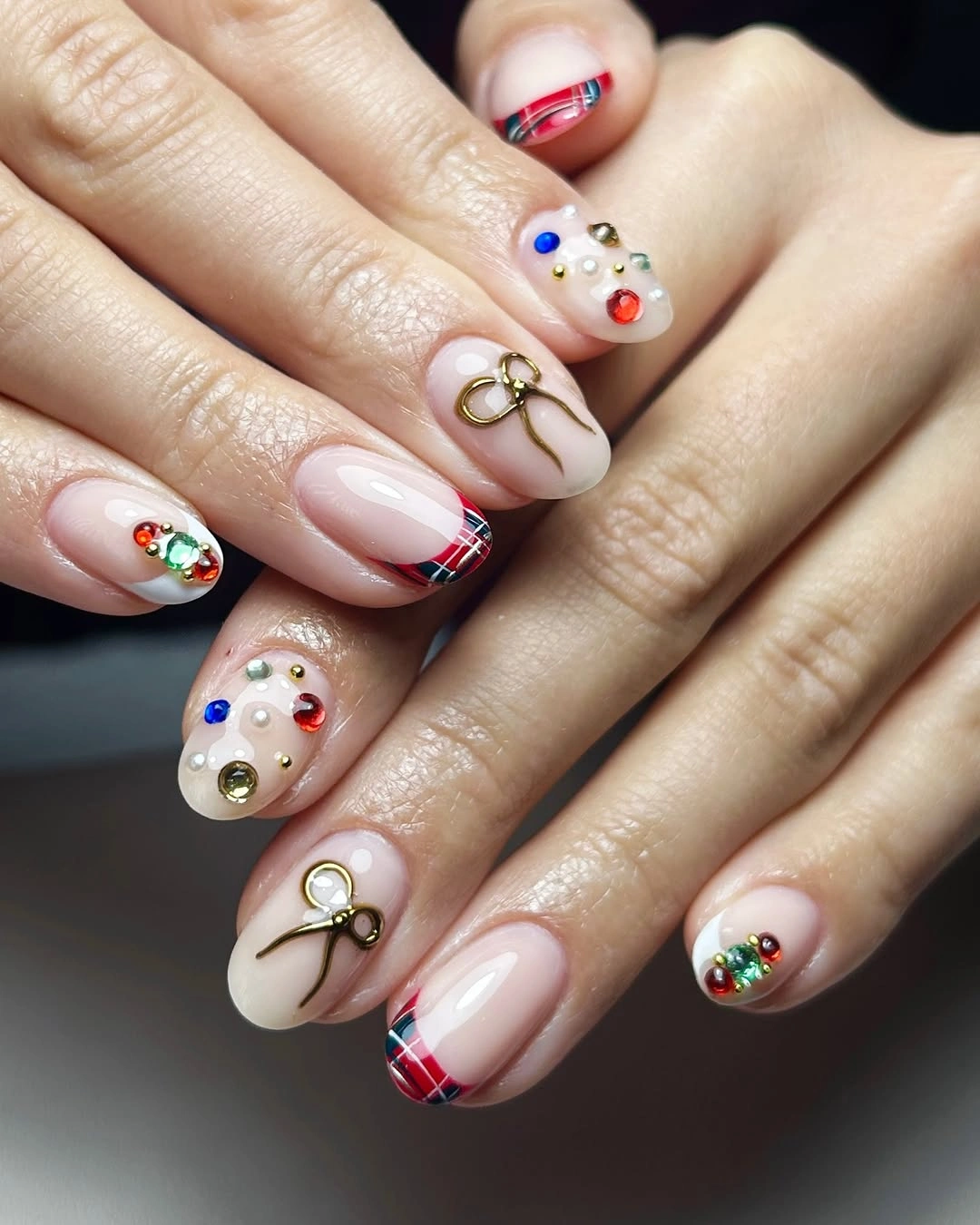 Nude pink nails with red plaid tips, gold bows and colorful embellishments