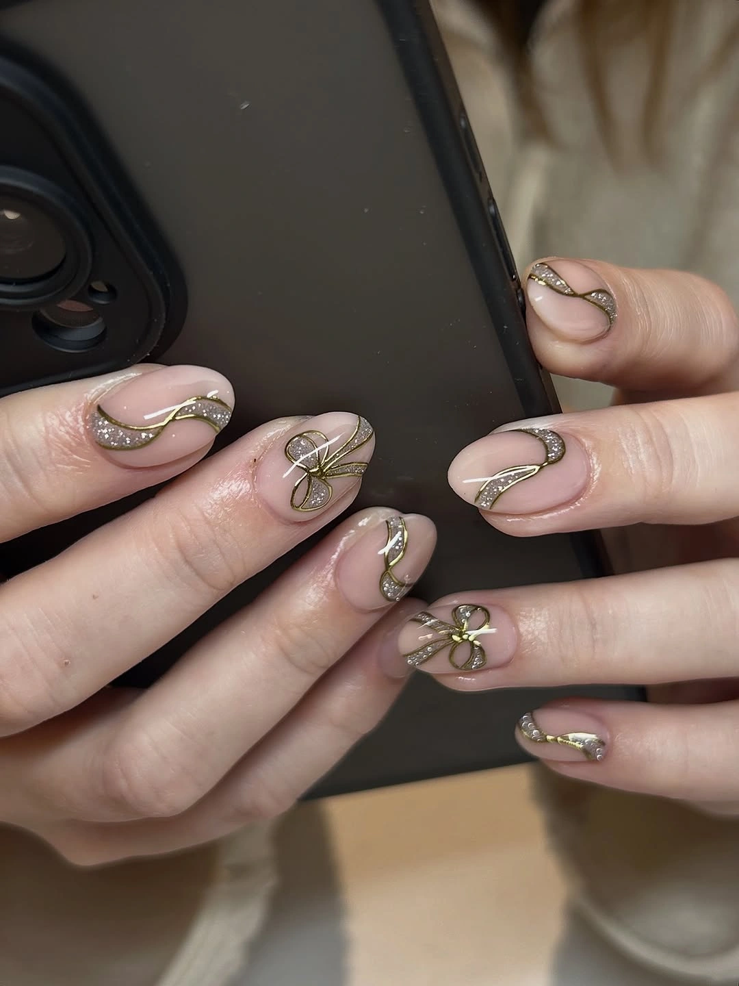Rounded nude pink nails with gold curves and delicate ribbon bows