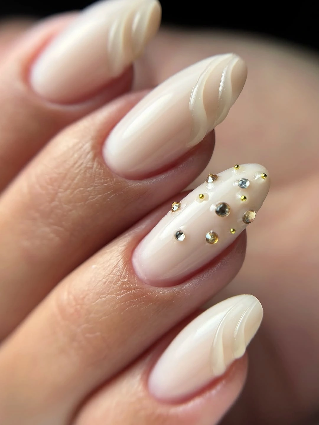 Almond cream nails with raised-looking curves and scattered gold-toned gems