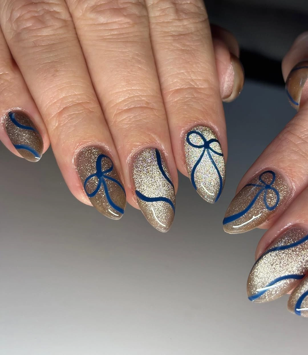 Champagne silver glitter almond nails decorated with deep blue ribbon bows