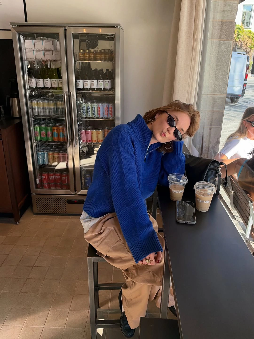 Oversized cobalt blue collared sweater with relaxed tan trousers and sunglasses