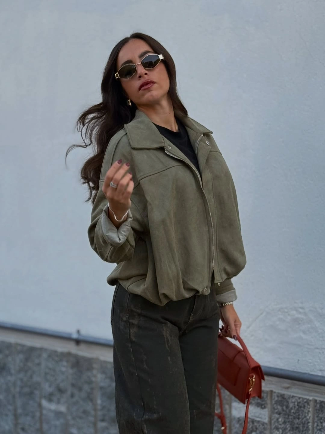 Muted olive jacket with charcoal jeans and reddish brown handbag