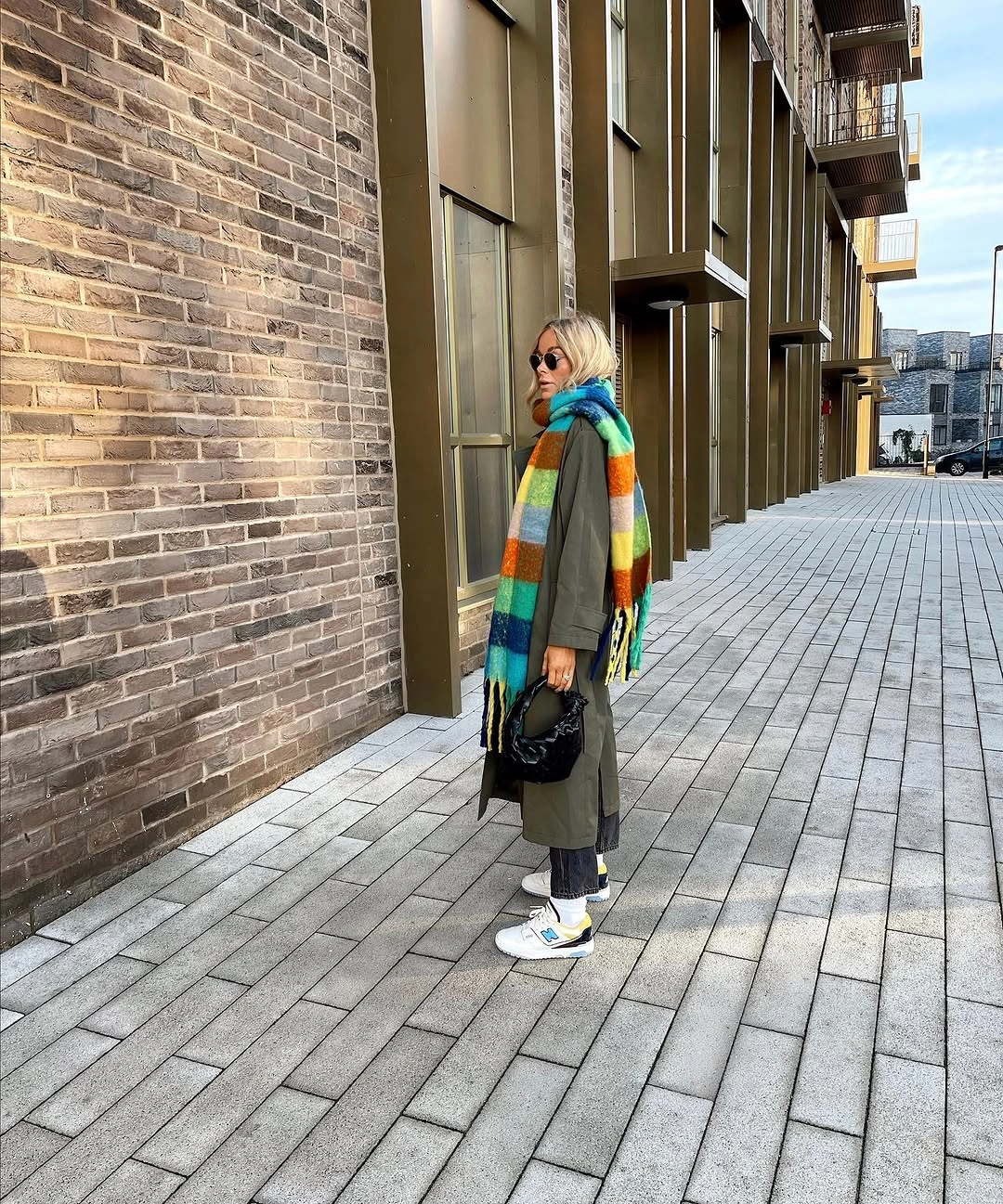 Long olive coat with multicolored striped scarf and pale sneakers