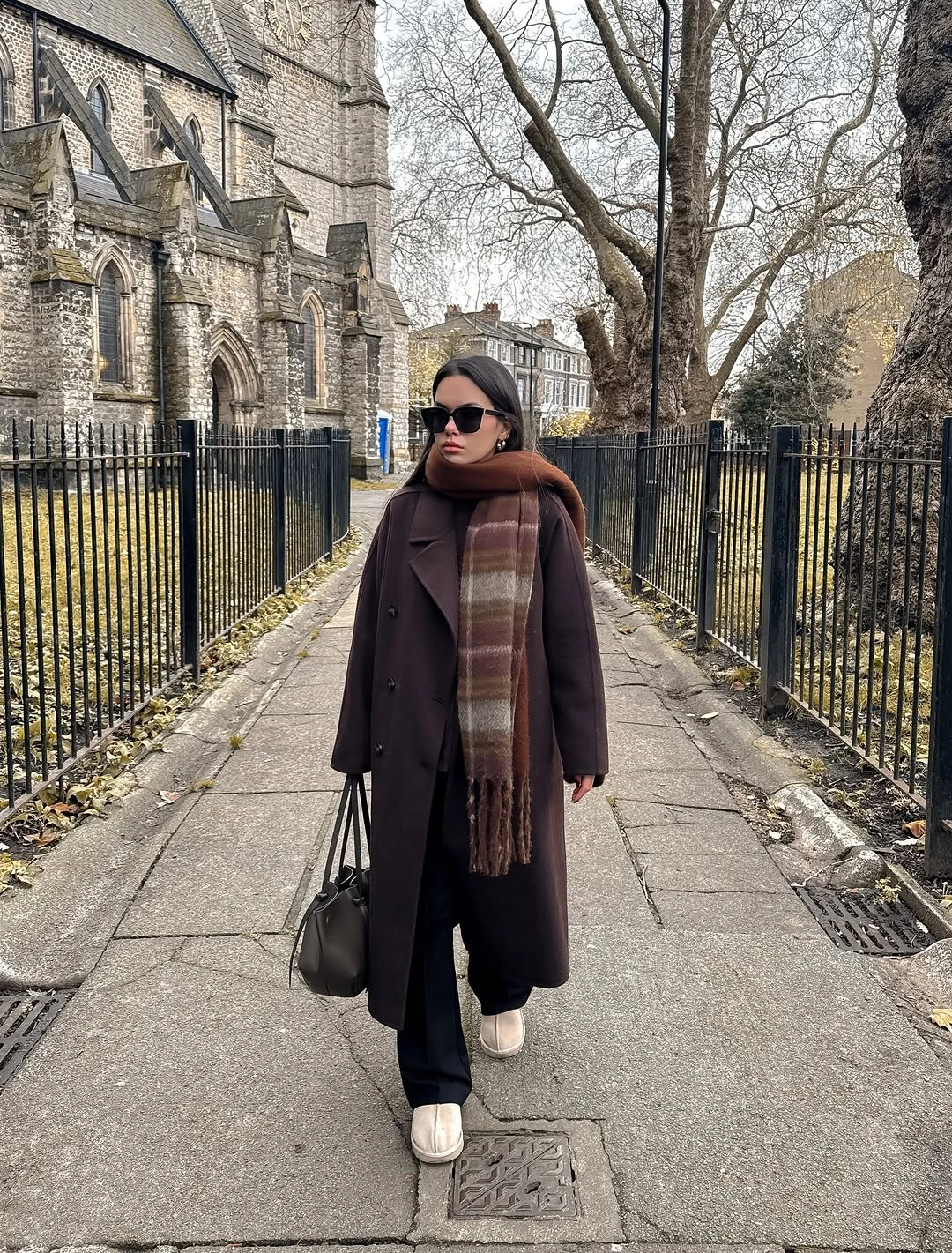 Long dark brown coat with plaid scarf and loose black trousers