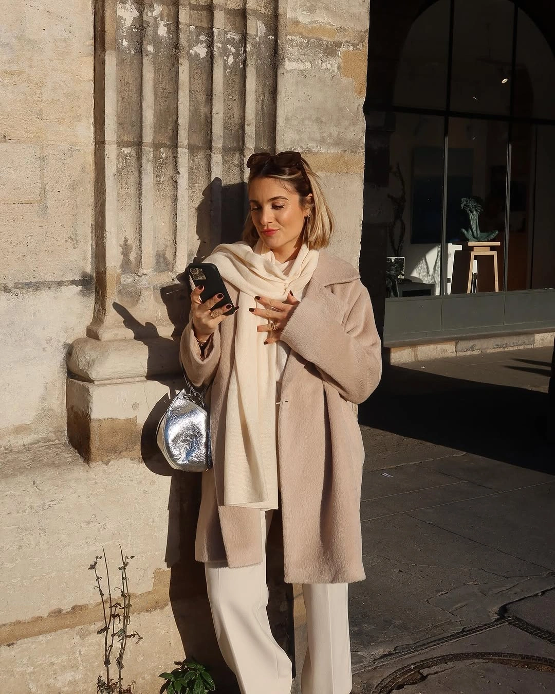 Taupe winter coat with cream scarf wide leg trousers and silver bag